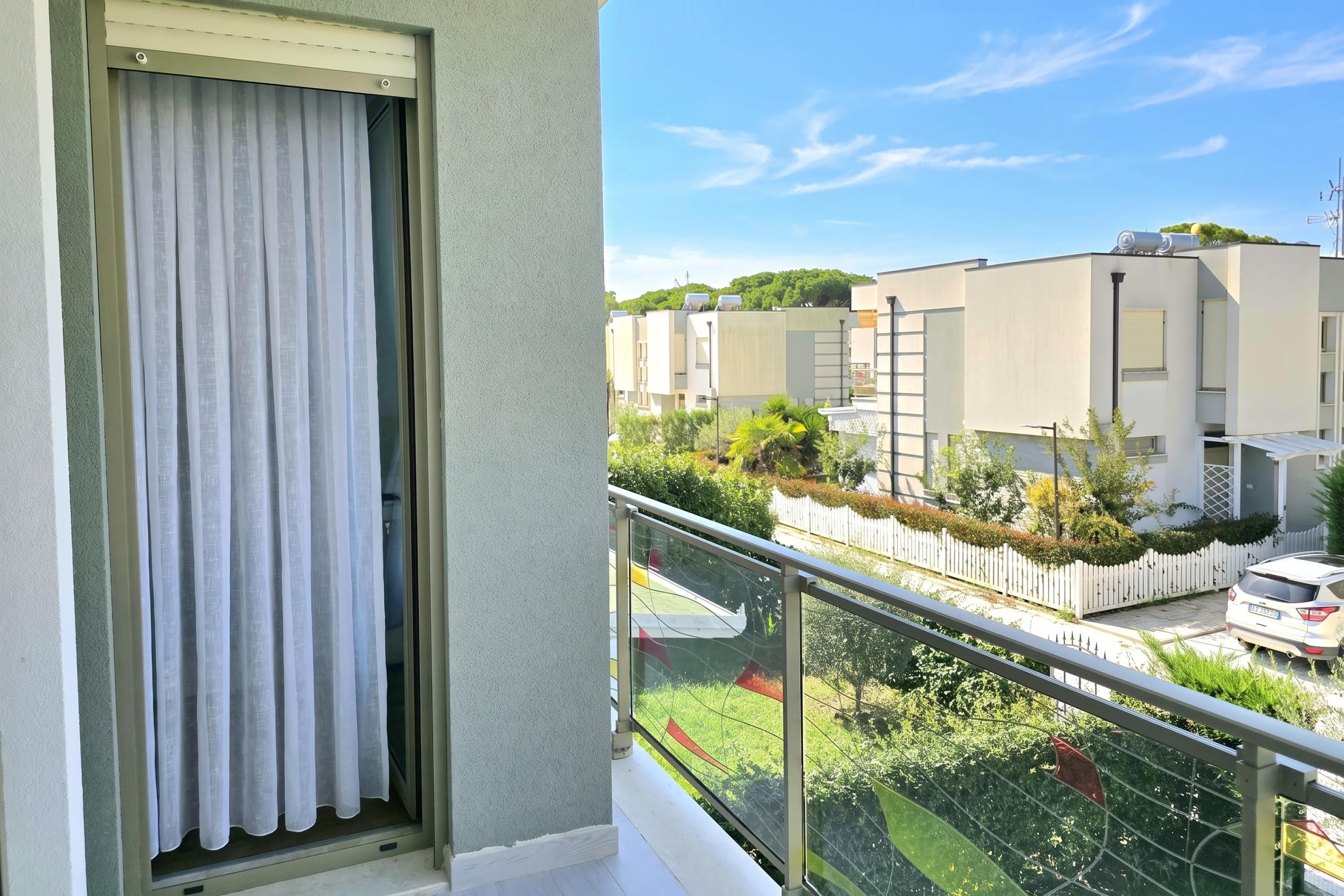 Un balcon donnant sur un quartier résidentiel, avec des maisons et une voiture blanche garée dans la rue.