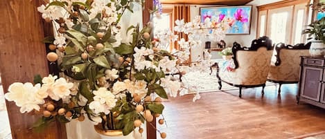 A room with a wooden ceiling, a ceiling fan, a white vase with flowers, and a patterned floor.