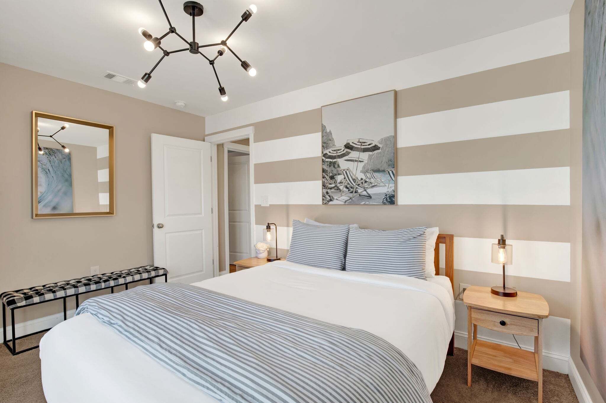 A bedroom with a bed, bedside tables, a bench, a ceiling light fixture, and a wall-mounted artwork.
