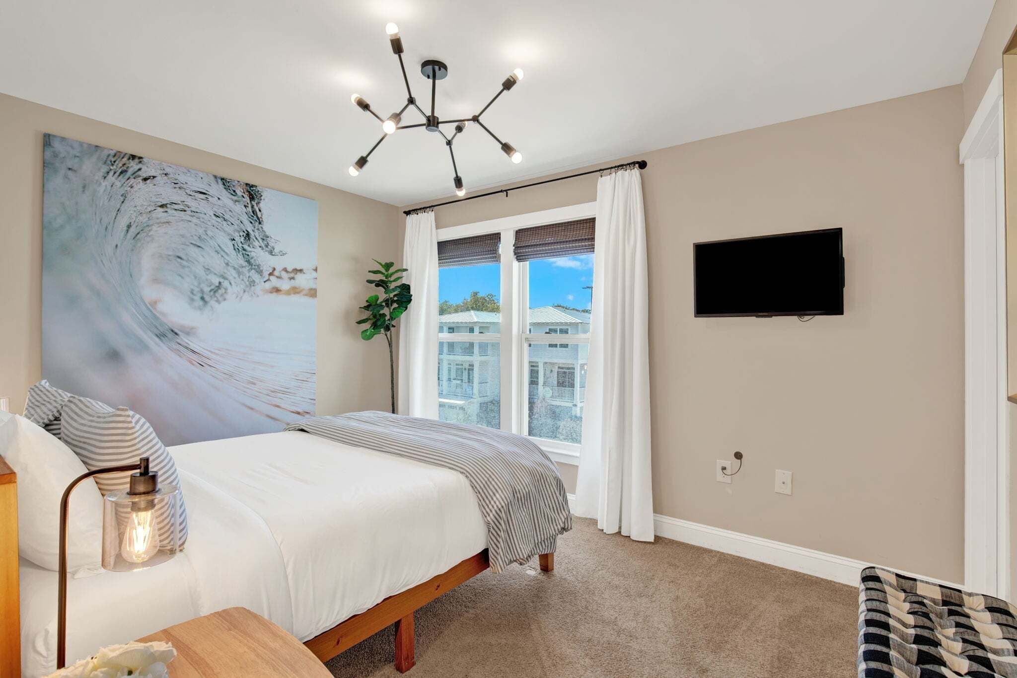 A bedroom with a bed, a TV, a large painting, and a window with curtains.