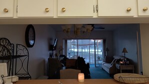 Huone, jossa on valkoiset kaapit, kattokruunu, ruokapöytä, jossa on kynttilä, ja näkymä lasiovesta.