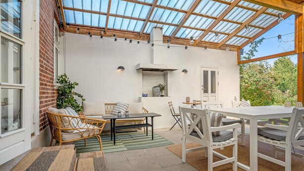 Een overdekt terras met een tafel en stoelen, een bakstenen muur en een raam.