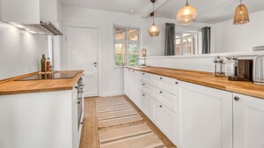 Een keuken met witte kastjes, houten aanrecht, een raam met gordijnen en hangende pendelverlichting.