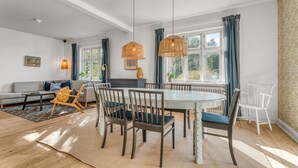 Een moderne woonkamer met een bank, eettafel, stoelen en een groot raam met gordijnen.