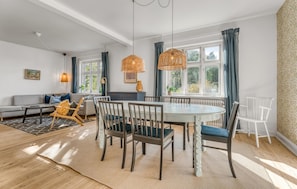 A modern living room with a sofa, dining table, chairs, and a large window with curtains.