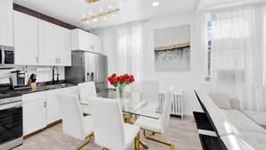A modern kitchen with white cabinets, stainless steel appliances, and a glass dining table with white chairs. - Luxury 4BR Sleeps 16 • Free Parking • Walk to Train • Near NYC (Yonkers)
