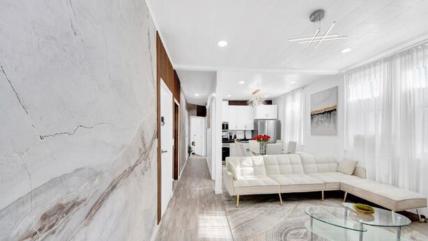 A modern living room with a sectional sofa, a glass coffee table, and a kitchen in the background. - Luxury 4BR Sleeps 16 • Free Parking • Walk to Train • Near NYC (Yonkers)