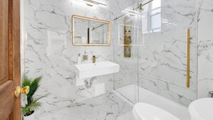 Een badkamer met marmeren wanden, een witte wastafel, een spiegel, een douche en een toilet.