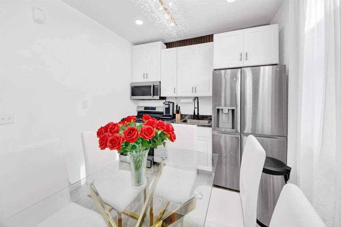 A modern kitchen with white cabinets, stainless steel appliances, and a glass dining table with a vase of red roses.
