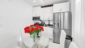 A modern kitchen with white cabinets, stainless steel appliances, and a glass dining table with a vase of red roses. - Luxury 4BR Sleeps 16 • Free Parking • Walk to Train • Near NYC (Yonkers)