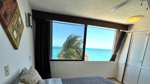 Ein Schlafzimmer mit einem Bett, einem Deckenventilator, einem Fenster mit Meerblick und einer Tür mit Klappläden.