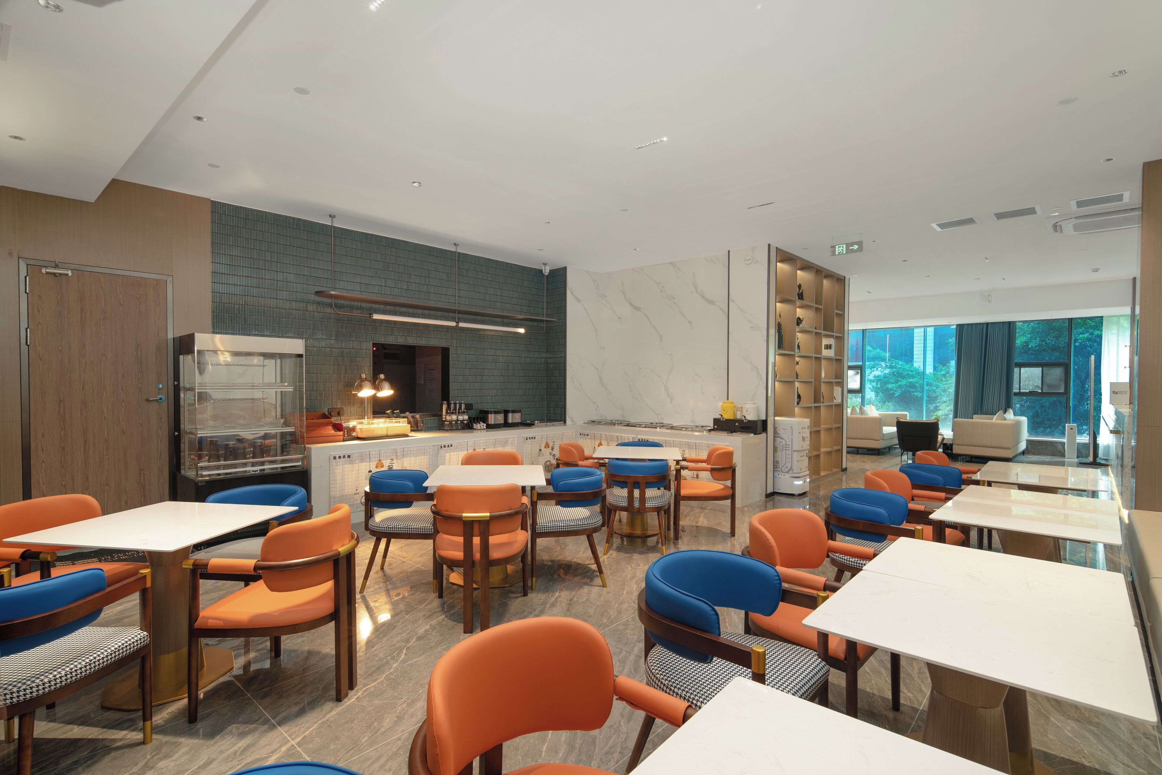 A modern restaurant with tables and chairs, a kitchen area, and a view of the outdoors.