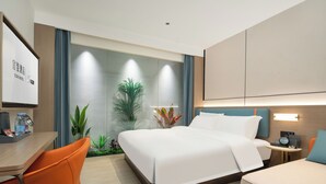 Ein Hotelzimmer mit Bett, Schreibtisch, Stuhl, Nachttisch mit einer Uhr und einem großen Fenster mit Vorhängen.