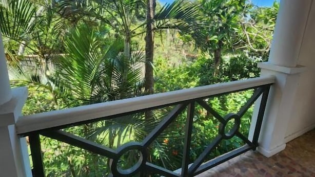A balcony with a tiled floor and a metal railing, overlooking a garden with various plants and trees. - La Marina Resort (Buzios)