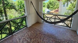 A balcony with a hammock, tiled floor, and a view of greenery and a building. - La Marina Resort (Buzios)