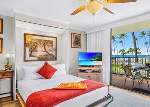 Habitación de hotel con cama, televisión, balcón y vista al océano, además de ventilador de techo.