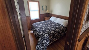 Een slaapkamer met een bed, raam, plafondventilator en nachtkastje.