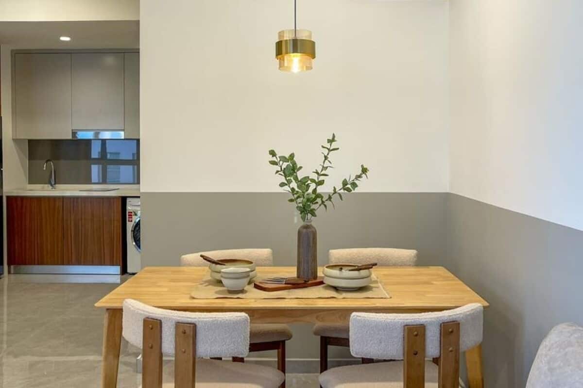 A modern dining area with a wooden table, four chairs, a vase with greenery, and a pendant light.