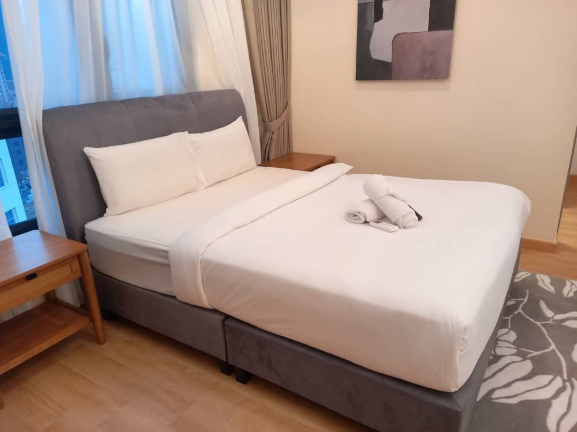 A neatly made bed with white linens, a wooden nightstand, and a small table beside it.