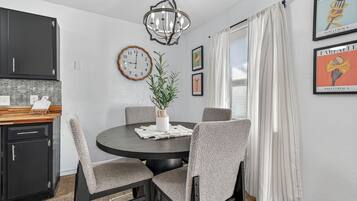 A dining area with a round table, chairs, a clock, and framed pictures on the wall.