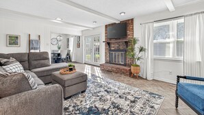 A spacious living room with a grey sofa, a patterned rug, a fireplace, and a dining area with a table and chairs. - Beautiful Meandering Way Retreat (Fort Smith)