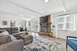 Ein geräumiges Wohnzimmer mit grauem Sofa, einem gemusterten Teppich, einem Kamin und einem Essbereich mit Tisch und Stühlen.