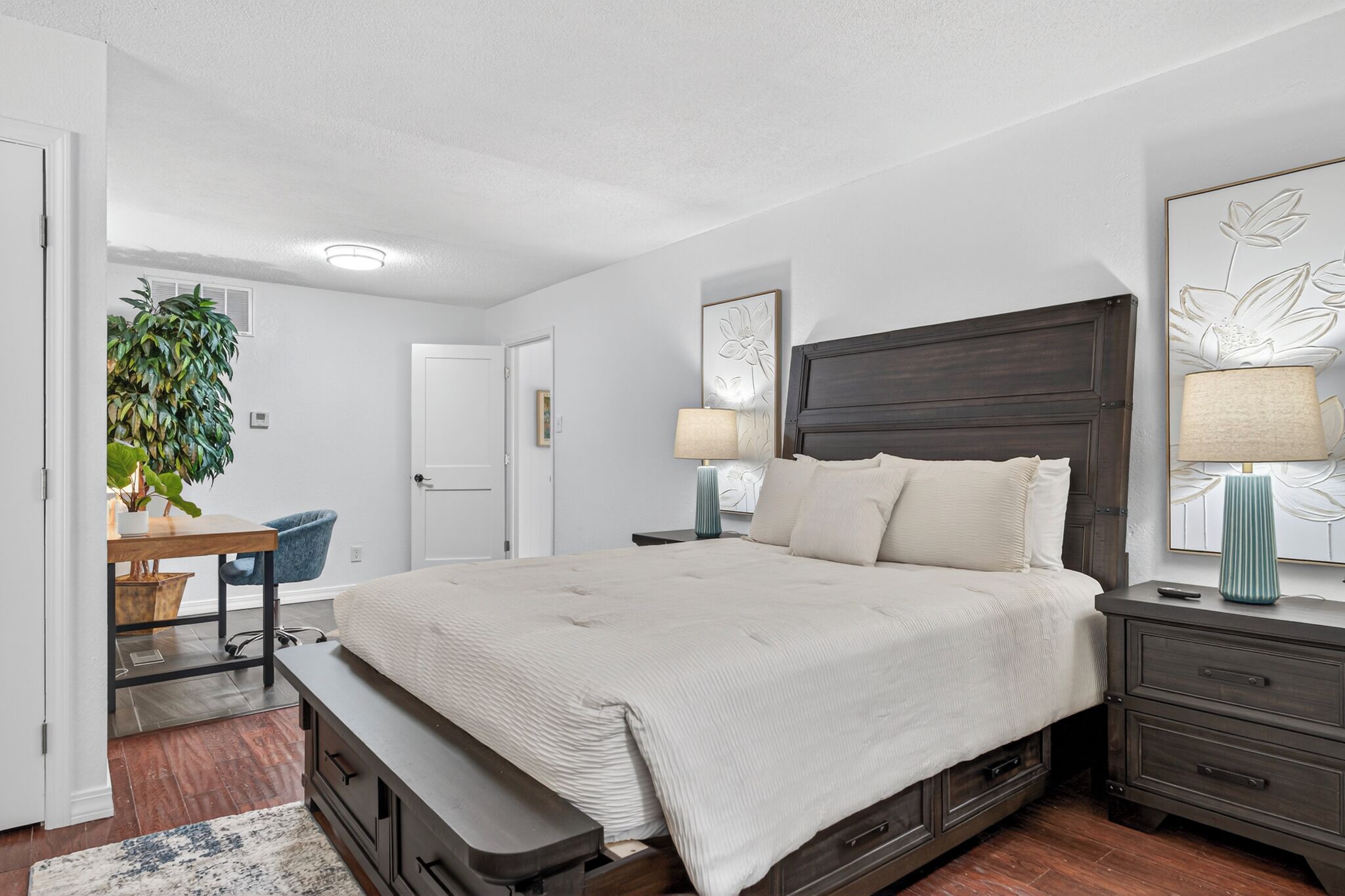 A bedroom with a large bed, bedside tables, a desk, and a potted plant.