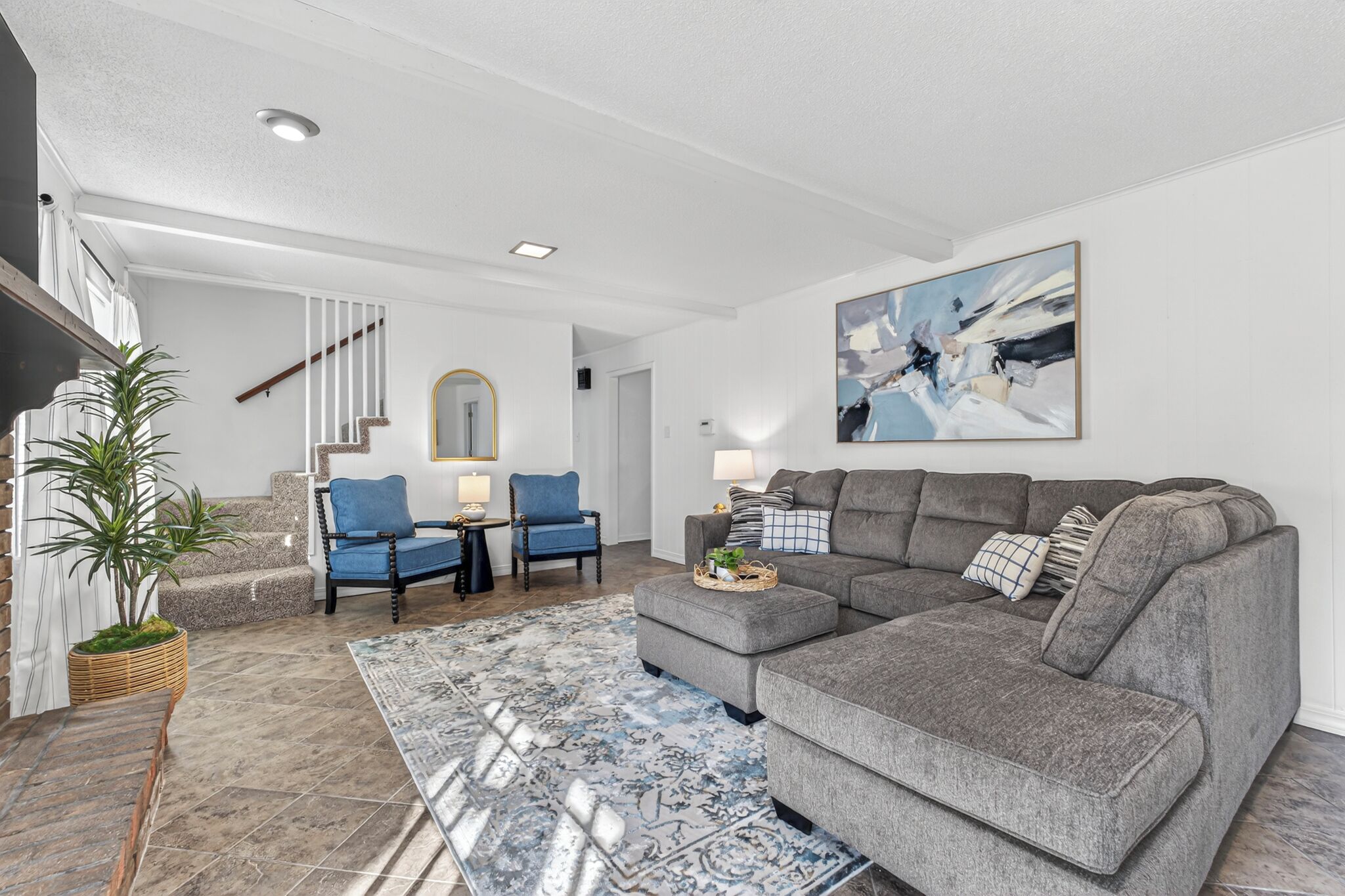 A modern living room with a grey sectional sofa, a blue armchair, and a patterned rug.