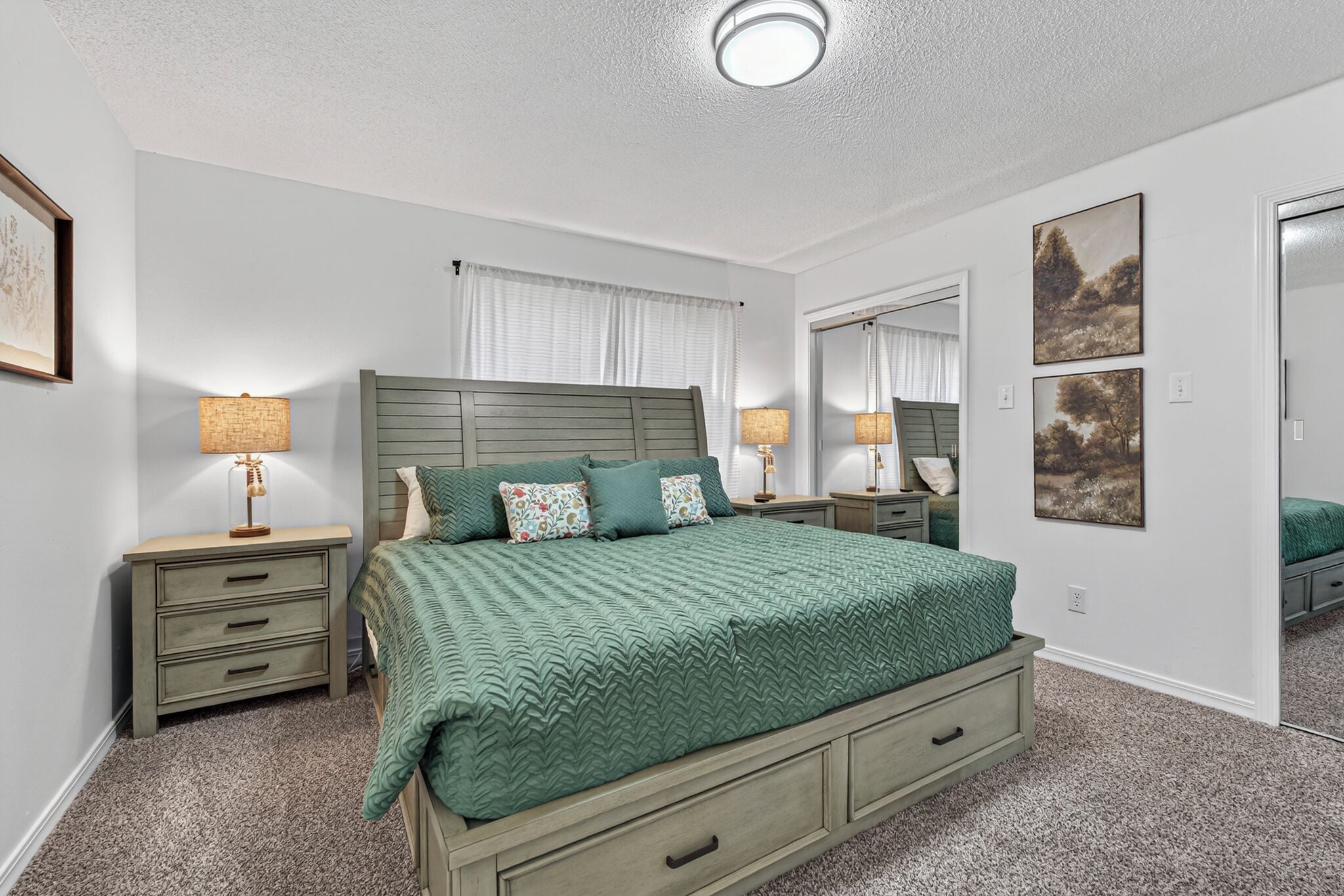 A bedroom with a bed, two bedside tables, a nightstand, a dresser, a mirror, and a ceiling light.