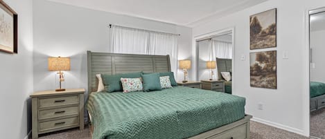 A bedroom with a bed, two bedside tables, a nightstand, a dresser, a mirror, and a ceiling light.