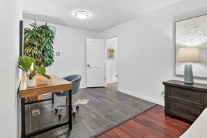 Ein Zimmer mit Schreibtisch, Stuhl, Blumentopf und Kommode.