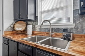 A kitchen with a double stainless steel sink, wooden countertop, and a window with blinds.