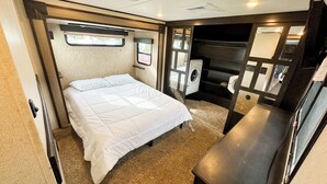 Dormitorio compacto en una autocaravana con cama, lavadora pequeña y una kitchenette compacta.