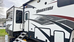 Una caravana grande con la marca 'Grand Design', una puerta corrediza y una rampa para accesibilidad.