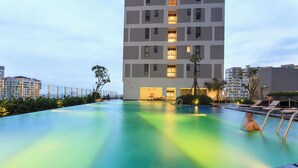 A swimming pool with a person in the water, surrounded by lounge chairs and a building with multiple floors and balconies. - RiverGate Saigon (Ho Chi Minh City)