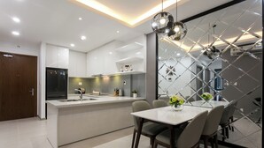 A modern kitchen with white cabinetry, a central island, and a dining area with a table and chairs. - RiverGate Saigon (Ho Chi Minh City)