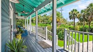 Eine überdachte Veranda mit Deckenventilator, Sitzgelegenheiten im Freien und Blick auf einen gepflegten Rasen und Palmen.