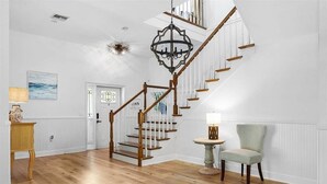 Eine Treppe mit Holzwerteln und einem Chandelier, ein Stuhl und ein Tisch mit einer Lampe.