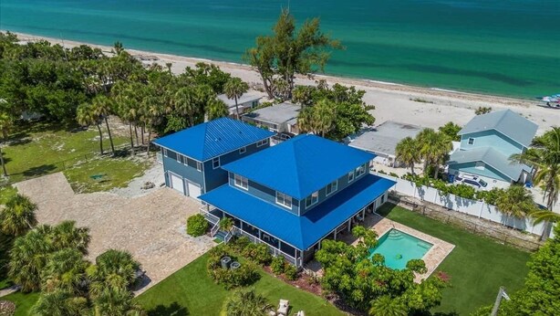 Ein zweistöckiges Haus mit blauem Dach, Swimmingpool und Blick auf den Strand.