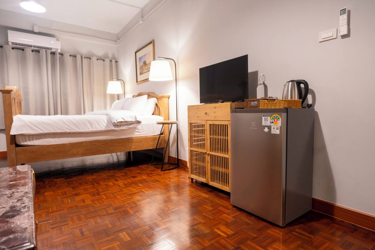 Une chambre d’hôtel équipée d’un lit, d’une commode en bois, d’une télévision, d’un réfrigérateur et d’un climatiseur fixé au mur.