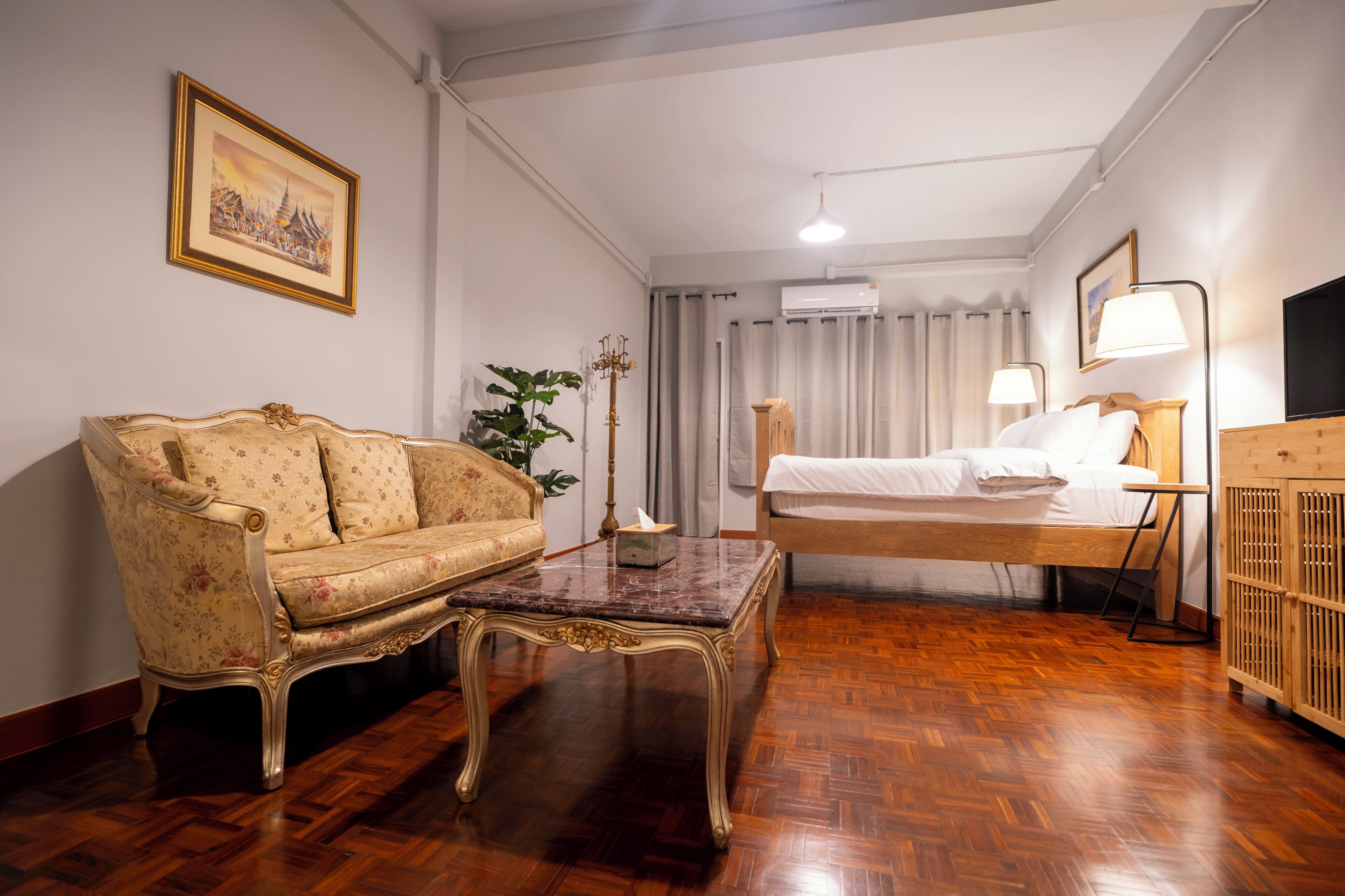 Una habitación con sofá, una mesita, una cama con cabecero de madera, televisor y lámpara.