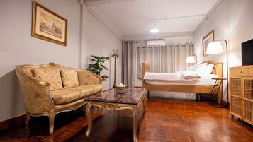 Una habitación con sofá, una mesita, una cama con cabecero de madera, televisor y lámpara.