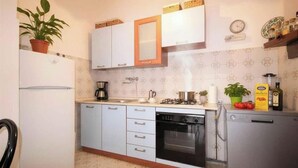 A compact kitchen with white cabinets, a refrigerator, a dishwasher, a stove, and a sink. - Holiday apartment mit Klimaanlage und Balkon (Diano Marina)