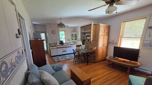 A living room with a sofa, TV, wooden floor, ceiling fan, kitchen in the background, and a dining area. - Mrs. Hippie Inn- Bluffside Suite near the Mississippi River in Alma, Wisconsin (Alma)