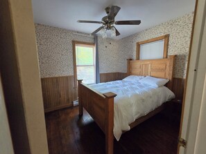 A bedroom with a wooden bed, a ceiling fan, and floral wallpaper.