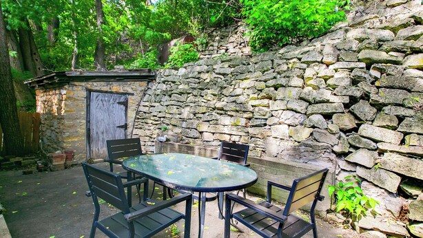 A stone wall, a wooden door, and a round table with chairs in a shaded outdoor area. - Mrs. Hippie Inn- Bluffside Suite near the Mississippi River in Alma, Wisconsin (Alma)