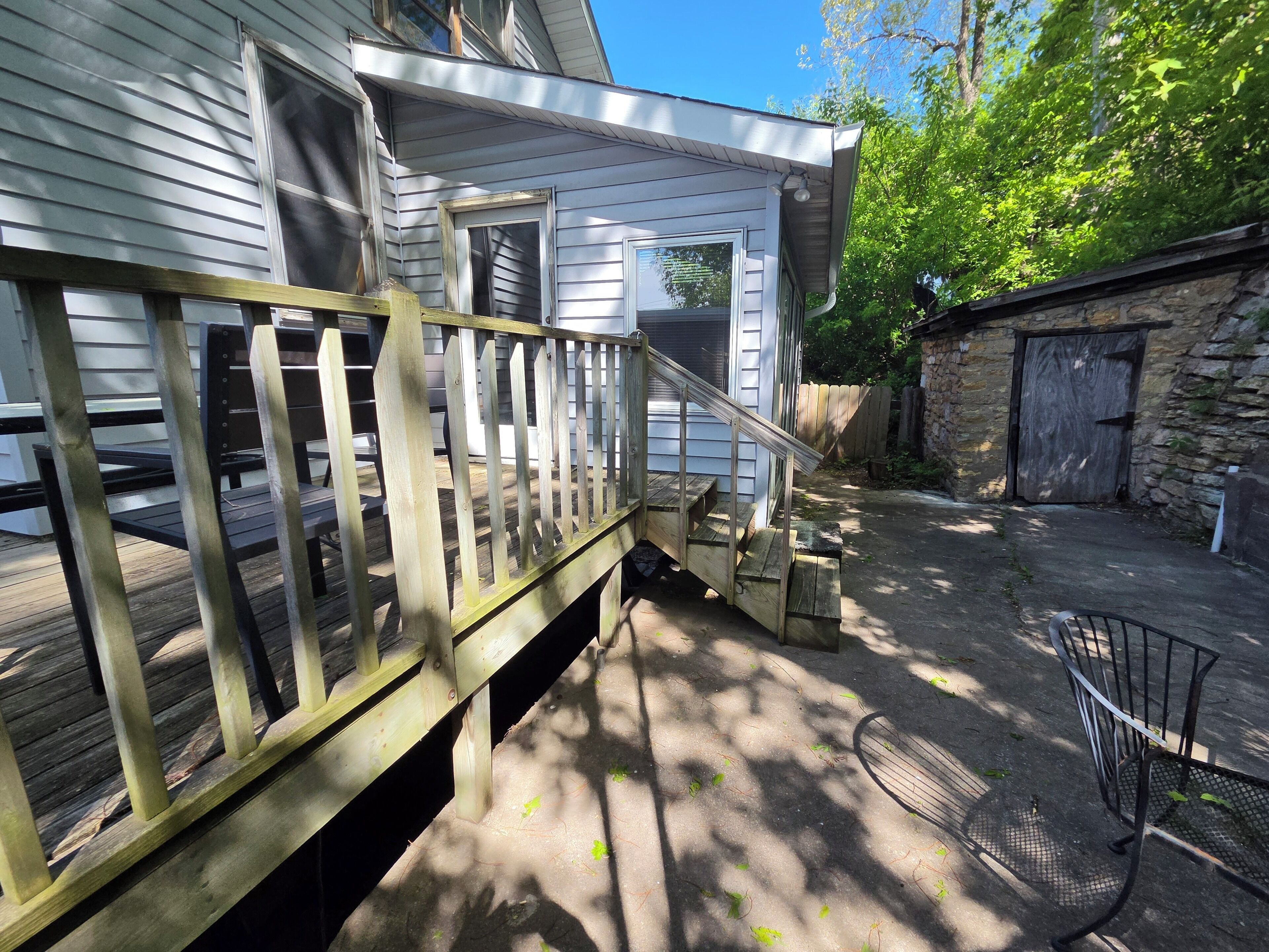 A wooden deck with a railing, a stone wall, and a metal chair.