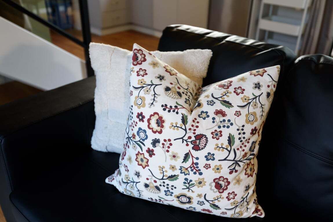A black leather sofa with two decorative pillows, one plain and one with a floral pattern.