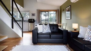 Ein modernes Wohnzimmer mit einem schwarzen Sofa, einem weißen Teppich, einem Essbereich mit Tisch und Stühlen sowie einer Treppe.