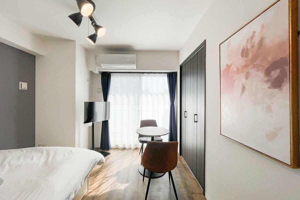 A hotel room with a bed, a desk, a chair, an air conditioning unit, and a large abstract painting on the wall.